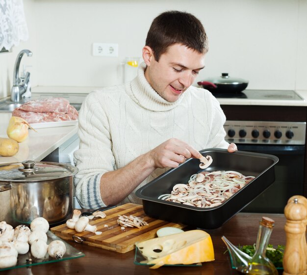 Hombre guapo cocinando carne con champiñones