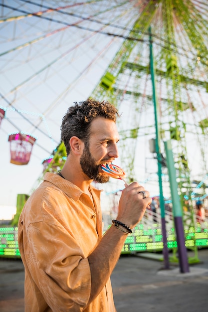 Foto gratuita hombre guapo comiendo chupetín en el parque de atracciones