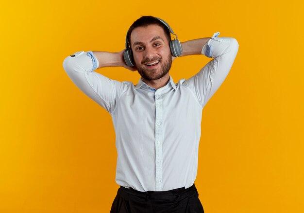 Hombre guapo complacido en auriculares sostiene la cabeza detrás con las manos aisladas en la pared naranja