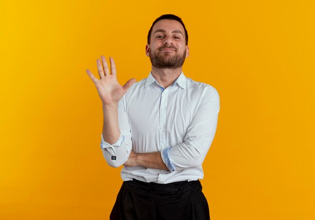 Hombre guapo complacido se encuentra con la mano levantada aislada en la pared naranja