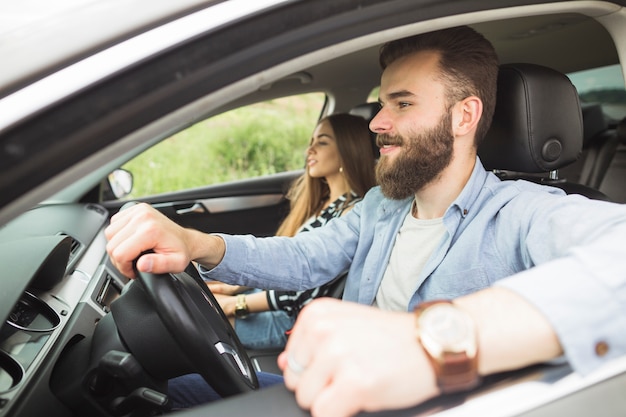 Hombre guapo conduciendo coche con su novia en el coche