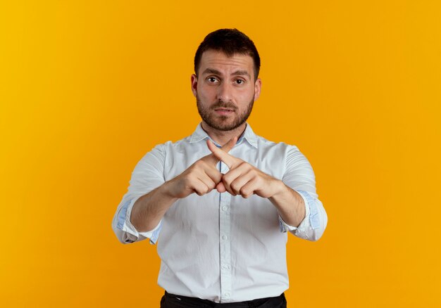 Hombre guapo confiado cruzando los dedos sin gesticular ningún signo aislado en la pared naranja