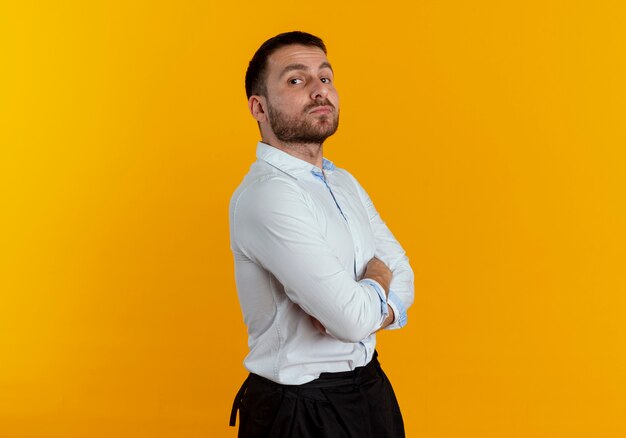 Hombre guapo confiado se encuentra de lado con los brazos cruzados mirando aislado en la pared naranja