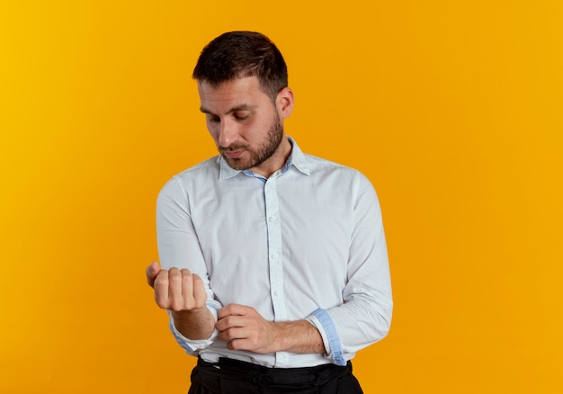 Hombre guapo confiado se enrolla las mangas aisladas en la pared naranja