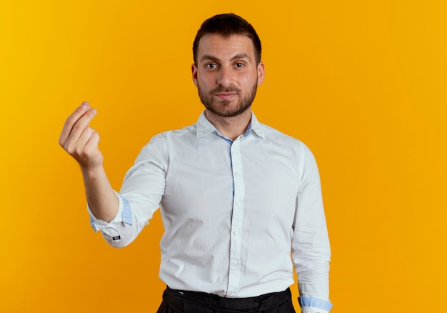 Hombre guapo confiado gestos dinero signo de mano aislado en la pared naranja