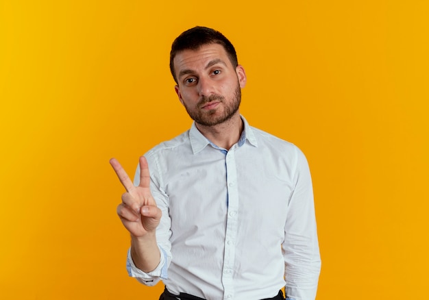 Hombre guapo confiado gestos signo de la mano de la victoria aislado en la pared naranja