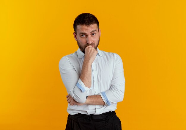 Hombre guapo confiado pone la mano en la barbilla mirando aislado en la pared naranja