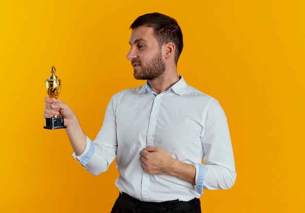 Foto gratuita hombre guapo confiado sostiene y mira la copa ganadora aislada en la pared naranja