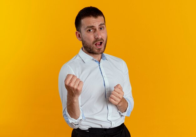 Hombre guapo confiado tiene puños aislados en la pared naranja