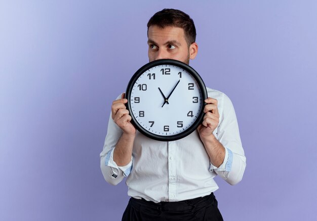 Hombre guapo confiado tiene reloj mirando al lado aislado en la pared púrpura