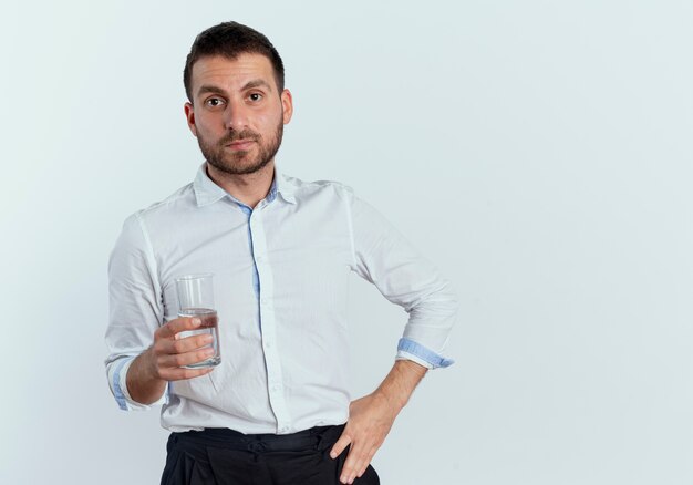 Hombre guapo confiado tiene vaso de agua aislado en la pared blanca