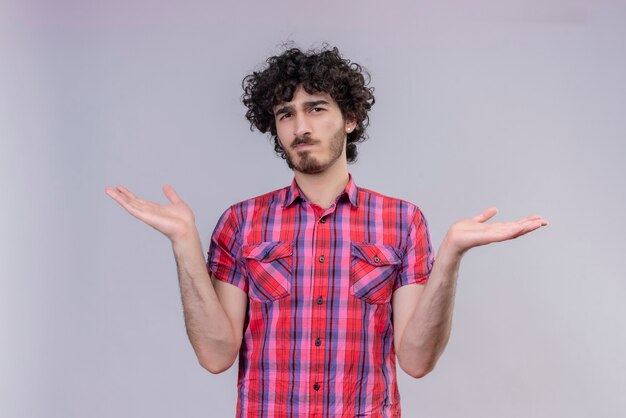 Un hombre guapo confundido con cabello rizado en camisa a cuadros, con los brazos abiertos