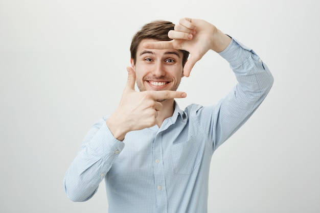 Hombre guapo creativo sonriendo, mostrando marcos de mano, momento de captura