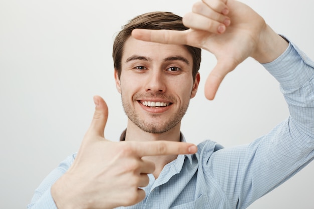 Hombre guapo creativo sonriendo, mostrando marcos de mano, momento de captura