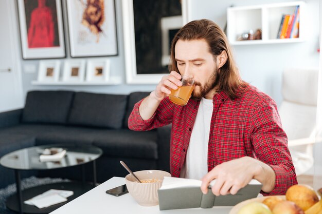 Hombre guapo desayunando y leyendo el libro en casa