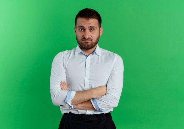 Hombre guapo disgustado se encuentra con los brazos cruzados aislados en la pared verde