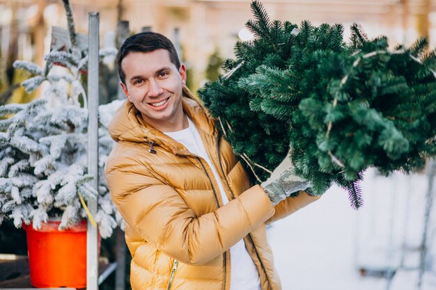 Hombre guapo eligiendo un árbol de navidad en un invernadero