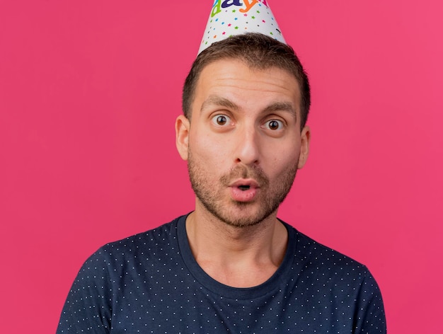 Hombre guapo emocionado con gorro de cumpleaños mira al frente aislado en la pared rosa con espacio de copia