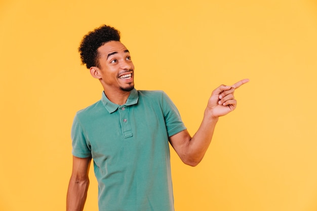 Hombre guapo emocionado en traje de moda dedo acusador. Filmación en interiores de maravilloso chico africano sonriente en camiseta verde.