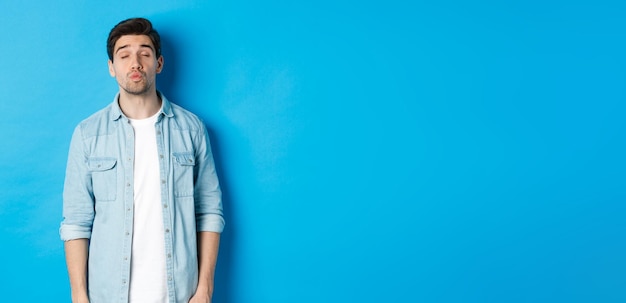 Foto gratuita hombre guapo esperando besar los labios fruncidos y cerrar los ojos mientras está de pie contra el fondo azul