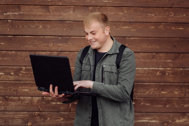 Hombre guapo está usando una computadora portátil y un teléfono al aire libre en la pared de madera