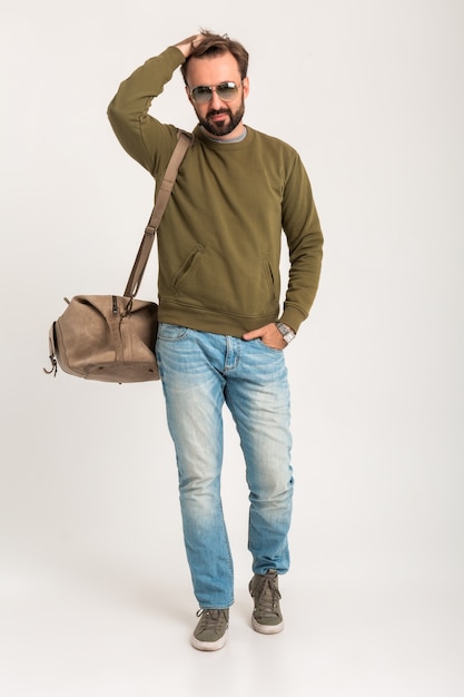 Foto gratuita hombre guapo con estilo barbudo posando aislado vestido con sudadera con bolsa de viaje, jeans y gafas de sol