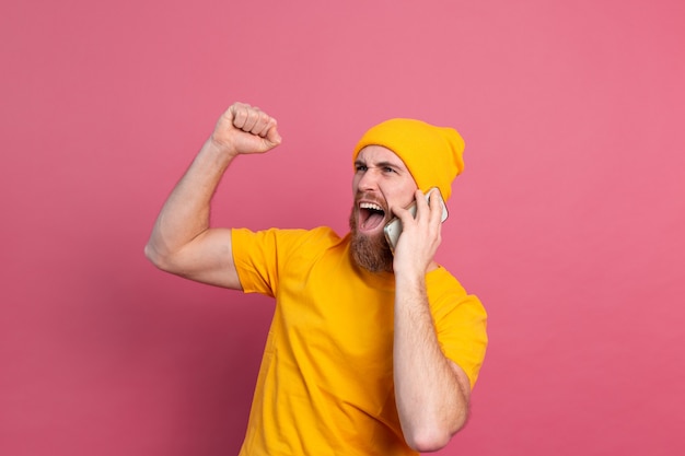 Hombre guapo europeo hablando por teléfono inteligente gritando orgulloso y celebrando la victoria y el éxito muy emocionado en rosa