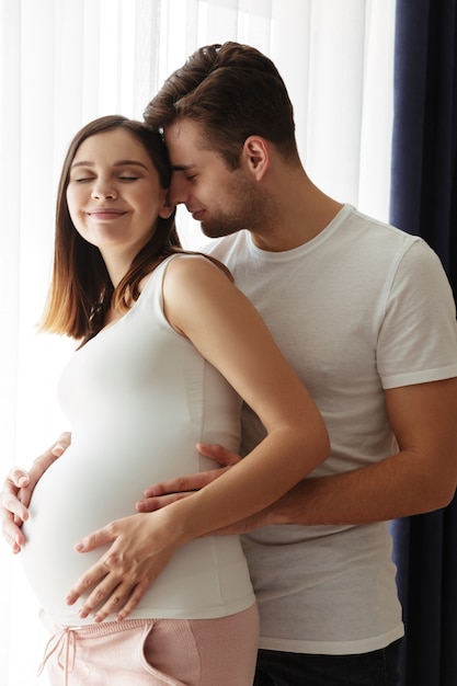 Hombre guapo feliz abraza a su encantadora esposa embarazada