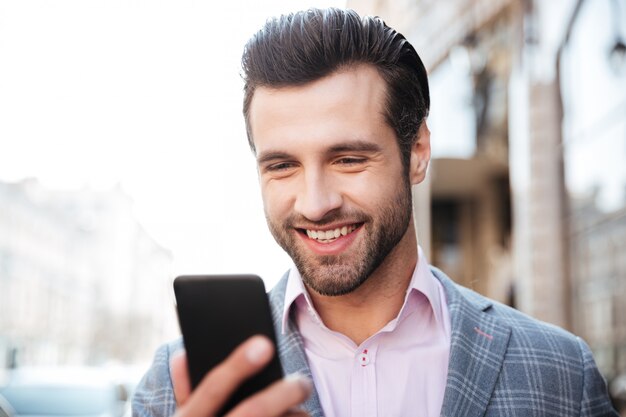 Hombre guapo feliz en chaqueta mirando teléfono móvil