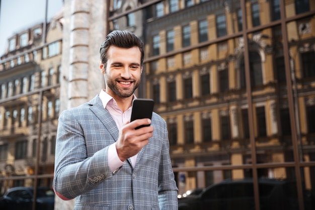 Hombre guapo feliz en chaqueta mirando teléfono móvil