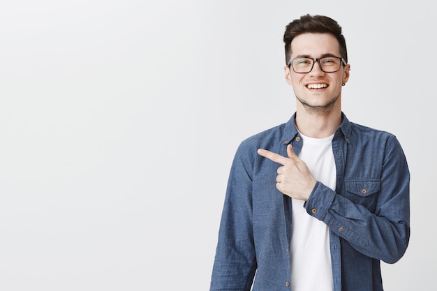 Hombre guapo feliz con gafas apuntando con el dedo a la izquierda