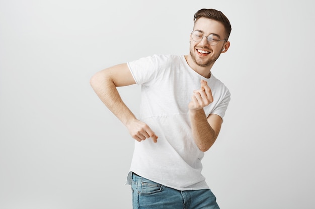 Hombre guapo feliz en gafas bailando, escuchando música en auriculares inalámbricos