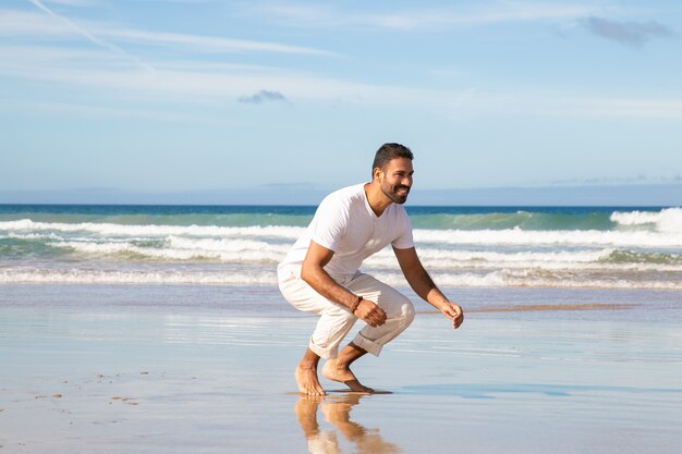 Hombre guapo feliz haciendo sentadillas y preparándose para atrapar y abrazar al niño