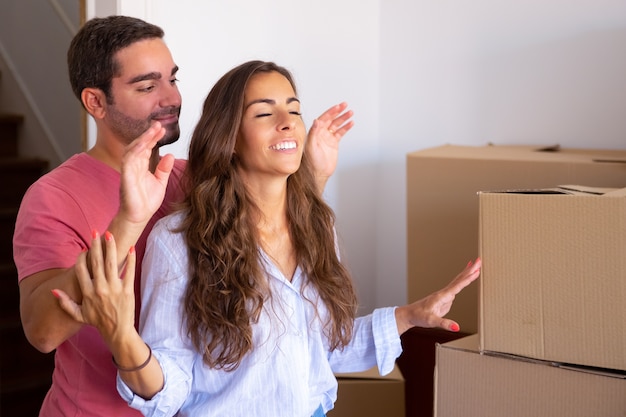 Hombre guapo feliz llevando a su novia con los ojos cerrados a su nuevo apartamento con cajas de cartón