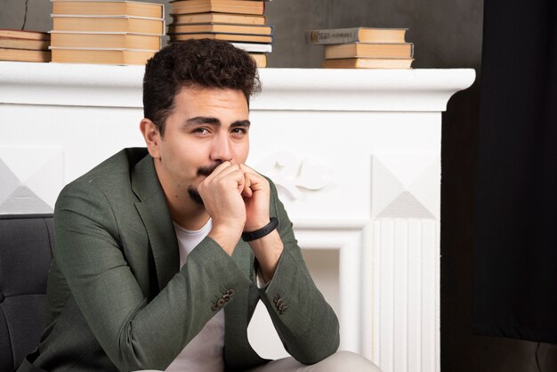 Hombre guapo feliz posando junto a la chimenea y libros