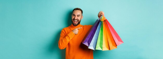 Hombre guapo feliz sosteniendo bolsas de compras y sonriendo señalando artículos comprados y recomendando st