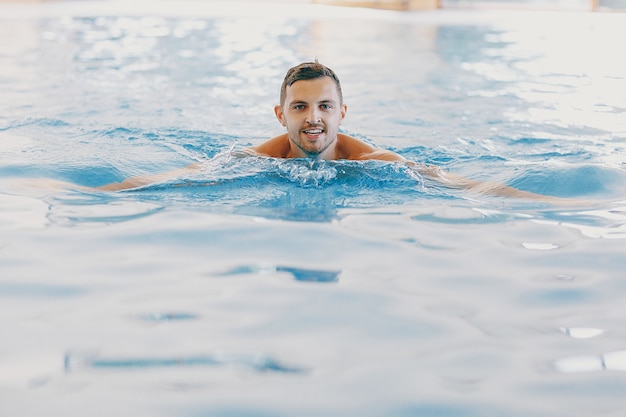 Un hombre guapo flotando en una gran piscina en casa