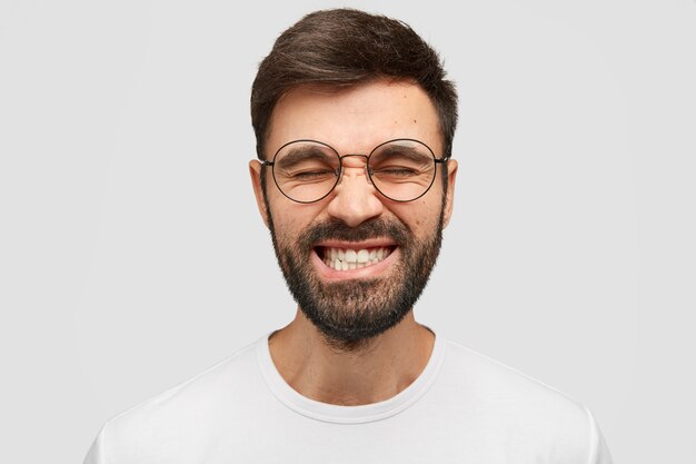 un hombre guapo frunce el ceño y aprieta los dientes, mantiene los ojos cerrados, intenta concentrarse en algo, usa una camiseta informal