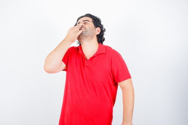 Hombre guapo fumando cigarrillo en camiseta roja y mirando serio. vista frontal.