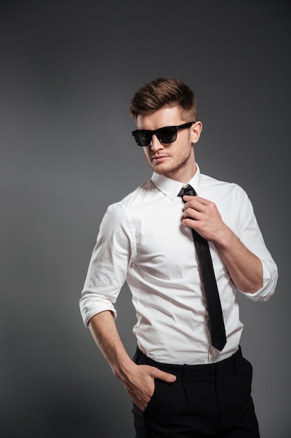 Hombre guapo en gafas de sol y ropa formal posando y mirando a otro lado