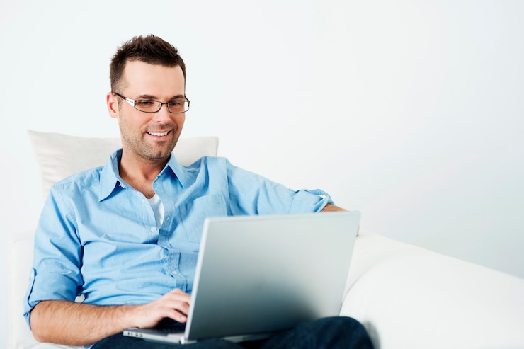 Foto gratuito hombre guapo con gafas usando una computadora portátil en el sofá