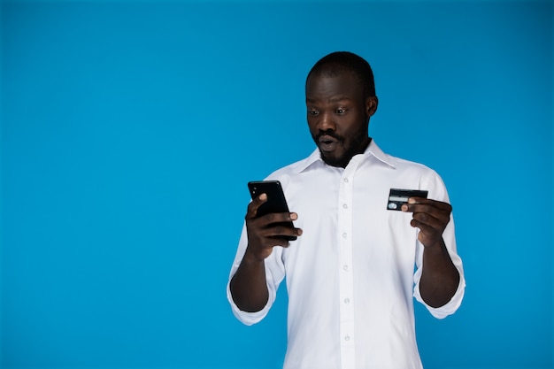 Hombre guapo gratamente sorprendido con una tarjeta de crédito y un teléfono