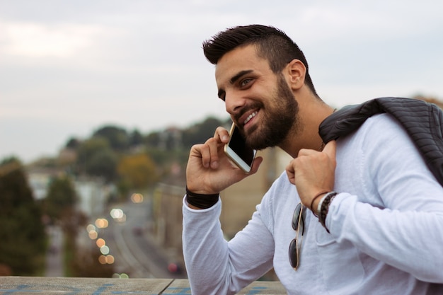 Hombre guapo hablando por teléfono al aire libre. Con chaqueta de cuero, gafas de sol, un tipo con barba. Efecto Instagram
