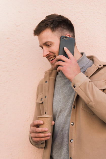 Hombre guapo hablando por teléfono y sosteniendo la taza de café