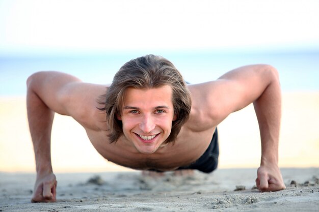 Hombre guapo haciendo flexiones en la playa