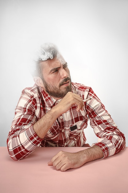 Foto gratuita hombre guapo hipster fumar cigarrillo en casa. hombre mirando hacia arriba y disfrutando de pasar el tiempo libre.