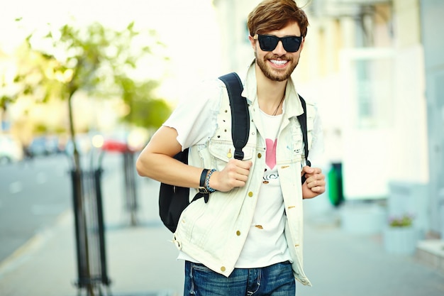 Hombre guapo inconformista sonriente divertido en tela elegante de verano en la calle con gafas de sol
