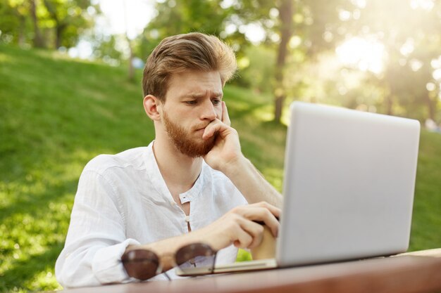 Hombre guapo jengibre maduro con computadora portátil en el parque