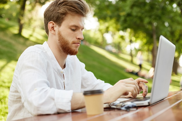 Hombre guapo jengibre maduro con computadora portátil en el parque