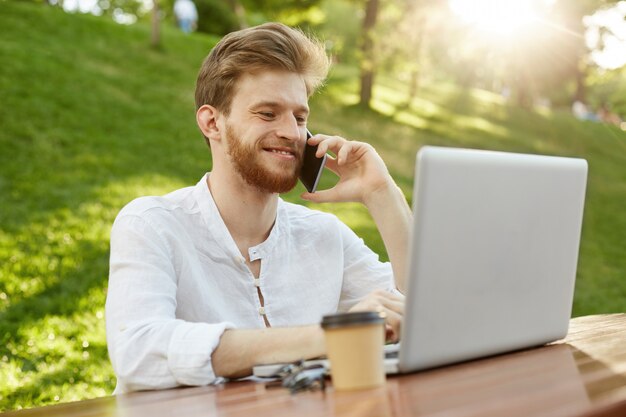 Hombre guapo jengibre maduro con computadora portátil en el parque